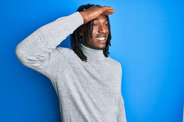 African american man with braids wearing turtleneck sweater very happy and smiling looking far away with hand over head. searching concept.