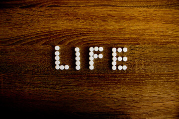The word life is lined with white pills on table.
