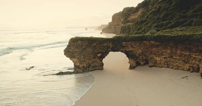 Sunrise of green cliff at ocean bay sand coast aerial view. Mesmerizing sun rize at Batu Bolong rock wall with giant hole at Bawana Beach, Sumba Island, Indonesia. Cinematic soft light drone shot