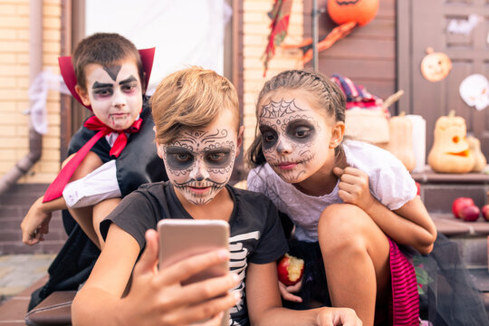 Cute boy with painted face making selfie with two friends in halloween costumes