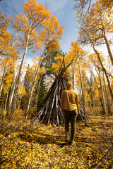 Woman Discovering Teepee in Woods Hiking on Trail Looking Up at Yellow Aspen Trees In Colorado...