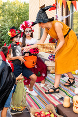 Young female in yellow dress and black witch hat bending in front of kids