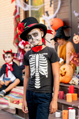 Cute boy with painted face in tee with skeleton and elegant hat looking at you