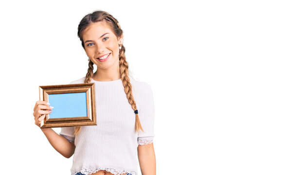 Beautiful caucasian woman with blonde hair holding empty frame looking positive and happy standing and smiling with a confident smile showing teeth