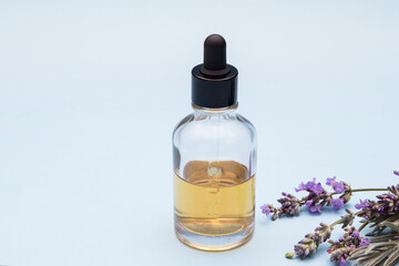 A glass bottle with a dropper filled with liquid on a blue background with lavender flowers.