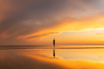 Silhouette of carefree fitness woman jumping on the beach at sunset, raising her hands up. Freedom concept. 
