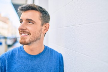 Young caucasian man smiling happy leaning on the wall at the city.