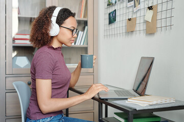 Young mixed-race female student in casualwear and headphones surfing in the net