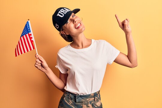 Young beautiful woman wearing usa cap holding united states flag smiling happy pointing with hand and finger to the side