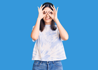 Young beautiful girl wearing casual t shirt doing ok gesture like binoculars sticking tongue out, eyes looking through fingers. crazy expression.