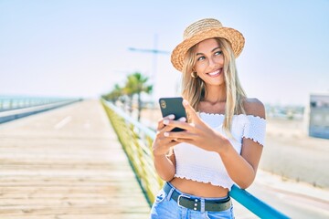 Young blonde tourist girl smiling happy using smartphone at the promenade.