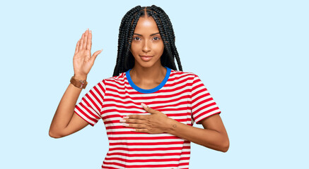 Beautiful hispanic woman wearing casual clothes swearing with hand on chest and open palm, making a...