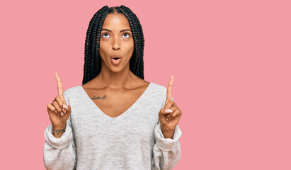 Beautiful hispanic woman wearing casual clothes amazed and surprised looking up and pointing with fingers and raised arms.