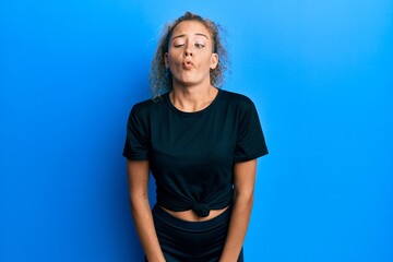 Beautiful caucasian teenager girl wearing black sportswear making fish face with lips, crazy and comical gesture. funny expression.