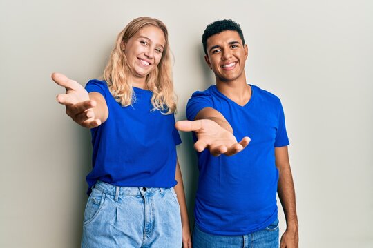 Young interracial couple wearing casual clothes smiling cheerful offering palm hand giving assistance and acceptance.