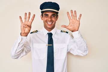 Young hispanic man wearing airplane pilot uniform showing and pointing up with fingers number nine while smiling confident and happy.