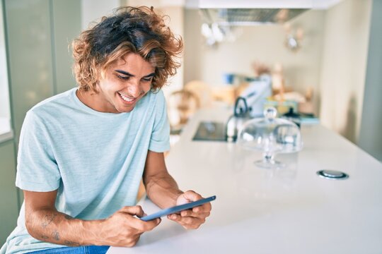 Young hispanic man smiling happy using touchpad sitting on the table at home
