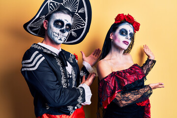 Young couple wearing mexican day of the dead costume over yellow inviting to enter smiling natural with open hand