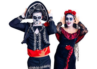 Young couple wearing mexican day of the dead costume over background smiling cheerful playing peek a boo with hands showing face. surprised and exited