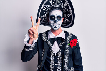 Young man wearing mexican day of the dead costume over white showing and pointing up with fingers...