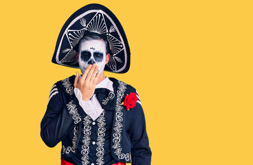 Young man wearing day of the dead costume over background bored yawning tired covering mouth with hand. restless and sleepiness.