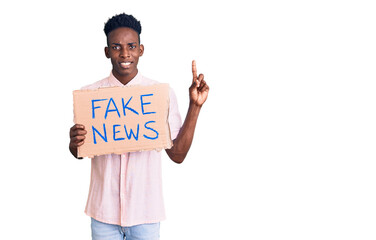 Young african american man holding fake news banner surprised with an idea or question pointing finger with happy face, number one