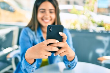 Young latin woman smiling happy using smartphone at coffee shop terrace.