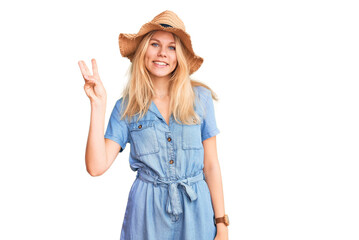 Obraz na płótnie Canvas Young beautiful blonde woman wearing summer hat and dress showing and pointing up with fingers number three while smiling confident and happy.