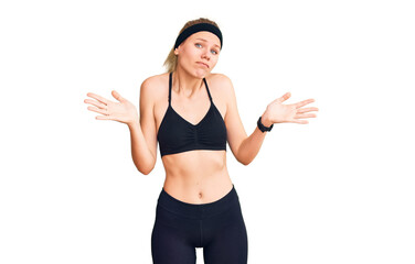 Young beautiful blonde woman wearing sportswear clueless and confused expression with arms and...