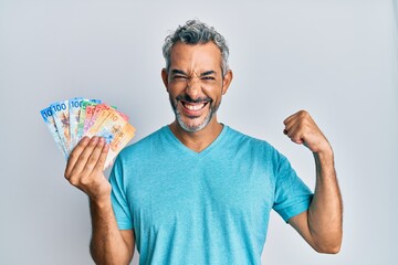 Middle age grey-haired man holding swiss franc banknotes screaming proud, celebrating victory and success very excited with raised arm