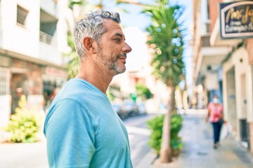 Middle age grey-haired man wearing casual clothes at street of city looking to side, relax profile pose with natural face with confident smile.