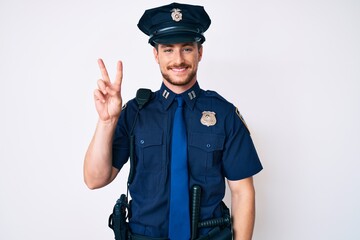 Young caucasian man wearing police uniform smiling looking to the camera showing fingers doing victory sign. number two.