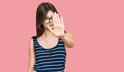 Young beautiful caucasian girl wearing casual clothes and glasses doing stop sing with palm of the...