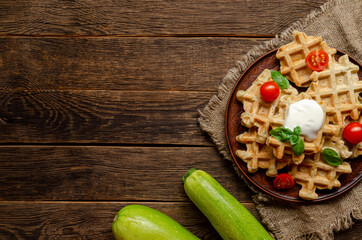 vegetarian zucchini waffles with herbs on a plate with fresh tomatoes, basil and sour cream on a wooden