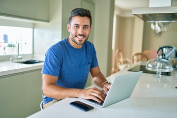 Fototapeta na wymiar Young handsome man smiling happy working using laptop at home