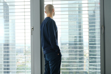 Fototapeta premium young man stands in an office in front of a window, looks at a modern European city, the concept of a business idea, a workplace