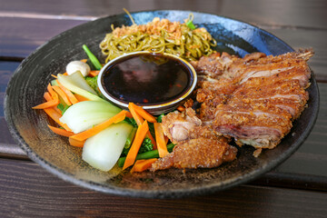 Asian dish with roasted duck, vegetables, noodles and teriyaki sauce in a flat bowl on a wooden table, selected focus