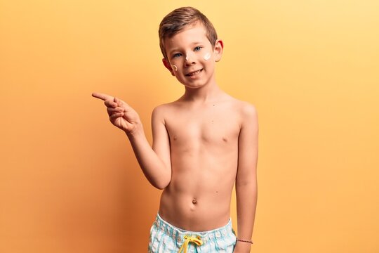 Cute blond kid wearing swimwear smiling happy pointing with hand and finger to the side
