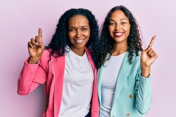 African american mother and daughter wearing business style smiling amazed and surprised and pointing up with fingers and raised arms.