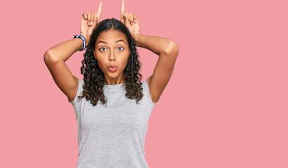 Young african american girl wearing casual clothes doing funny gesture with finger over head as bull horns
