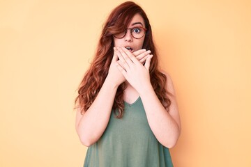 Young beautiful woman wearing casual clothes and glasses shocked covering mouth with hands for mistake. secret concept.