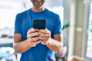 Young irish man smiling happy using smartphone standing at home.