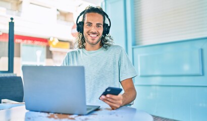 Young hispanic man smiling happy working using laptop and headphones at terrace of coffee shop.