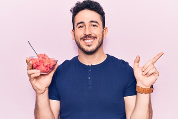 Young hispanic man holding ice cream smiling happy pointing with hand and finger to the side
