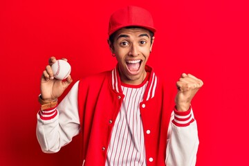 Young african amercian man wearing baseball uniform holding ball screaming proud, celebrating victory and success very excited with raised arms