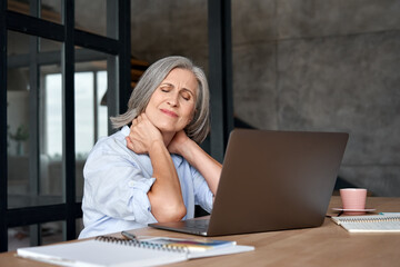 Tired stressed old mature business woman suffering from fibromyalgia neckpain working in office...