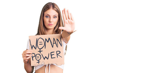 Young beautiful blonde woman holding woman power banner with open hand doing stop sign with serious...