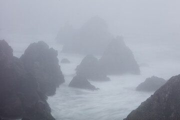 The Pacific Ocean crashes against sea stacks along the foggy seashore of Northern California. This...