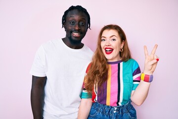 Interracial couple wearing casual clothes showing and pointing up with fingers number two while smiling confident and happy.