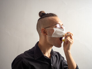 Young Blond Hair Caucasian Male in Black Shirt and Glasses Wears a Disposable Face Mask for Covid-19, Uses Salbutamol Inhalator for Asthma and Allergy Related Breathing Problems